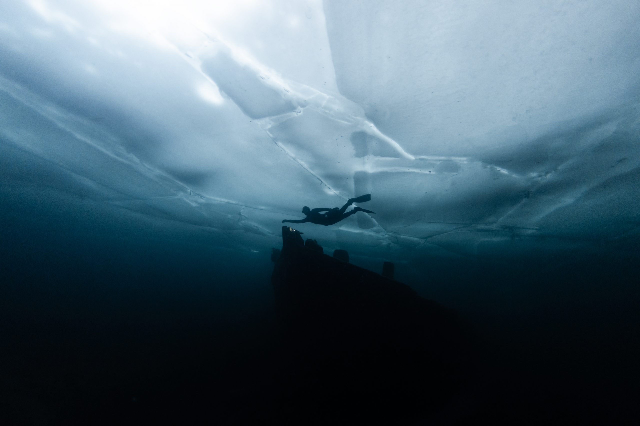 Silhouette en apnée sous glace au-dessus d'un bateau immergé